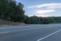 a motorcycle parked on the side of a highway near trees and a hill is seen from a moving vehicle