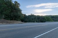 a motorcycle parked on the side of a highway near trees and a hill is seen from a moving vehicle