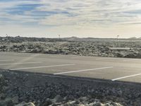 empty parking lot with white lines and rocky terrain in the background, with mountains in the distance