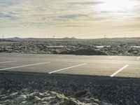 empty parking lot with white lines and rocky terrain in the background, with mountains in the distance