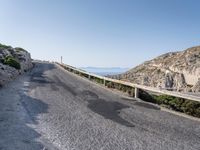 the road is covered with grey gravel and some rocks and mountains behind it is a steep rocky cliff