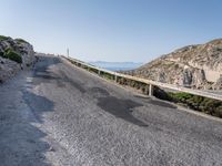 the road is covered with grey gravel and some rocks and mountains behind it is a steep rocky cliff