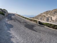 the road is covered with grey gravel and some rocks and mountains behind it is a steep rocky cliff