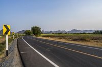 a road sign pointing right into the distance in front of mountains, fields, and a yellow arrow