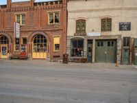 a red fire hydrant sitting in front of an old store window and building next to an open air field