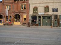 a red fire hydrant sitting in front of an old store window and building next to an open air field