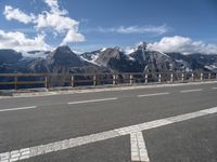 a road with a view of snow capped mountains in the distance and mountains below and a line of street markers painted on it