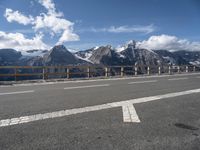 a road with a view of snow capped mountains in the distance and mountains below and a line of street markers painted on it