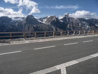 a road with a view of snow capped mountains in the distance and mountains below and a line of street markers painted on it