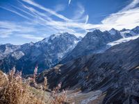 a road winding down a hill side with a mountainside behind it, with snow covered mountains in the background