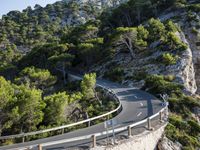 a curving highway going up the side of a mountain near water and a forest line