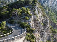 a curving highway going up the side of a mountain near water and a forest line