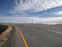 a paved road with mountains behind it on a clear day with clouds and yellow lines