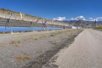 a long fence along a highway by the mountains has a large, bright blue pool of water in it