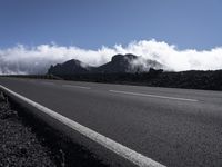 an asphalt road with a low laying line between it and the mountains with clouds in the distance