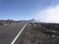 a road near the mountain side in the foggy sun day, and on the opposite bank are hills