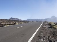 a road near the mountain side in the foggy sun day, and on the opposite bank are hills