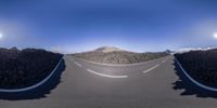 a road is curved between two bushes and mountains at different angles with some rocks surrounding