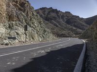 a curve road with an asphalt and rocky mountain behind it and blue sky overhead view