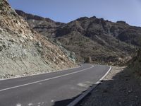 a curve road with an asphalt and rocky mountain behind it and blue sky overhead view