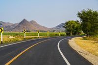 a black and yellow road sign on the middle of an empty highway surrounded by hills