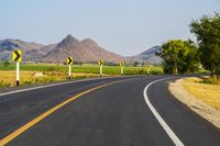 a black and yellow road sign on the middle of an empty highway surrounded by hills