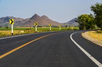 a black and yellow road sign on the middle of an empty highway surrounded by hills