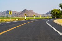 a black and yellow road sign on the middle of an empty highway surrounded by hills