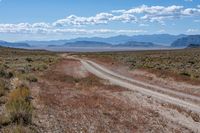 road through dry terrain in large open field with mountains in the distance next to a dirt road