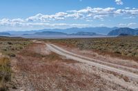 road through dry terrain in large open field with mountains in the distance next to a dirt road