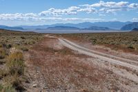 road through dry terrain in large open field with mountains in the distance next to a dirt road