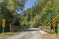 a paved road with wood bridges crossing over it, between the woods with trees and mountains