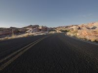 an empty paved road surrounded by mountain peaks and arid area, at sunset on a sunny day