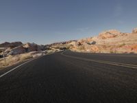 an empty paved road surrounded by mountain peaks and arid area, at sunset on a sunny day