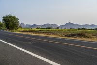 a wide open road with mountains in the distance and a line of trees along both sides