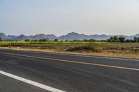 a wide open road with mountains in the distance and a line of trees along both sides