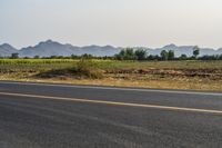 a wide open road with mountains in the distance and a line of trees along both sides