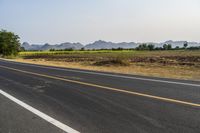 a wide open road with mountains in the distance and a line of trees along both sides