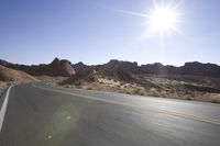 there is a motorcycle driving on a desert road, with sun shining on the street