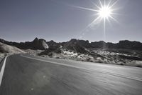 there is a motorcycle driving on a desert road, with sun shining on the street