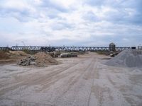 dirt road that has truck parked along it near a building and bridge over the water