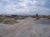 dirt road that has truck parked along it near a building and bridge over the water