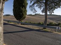 an empty country road near rolling hills and a fenced in area with grass and trees