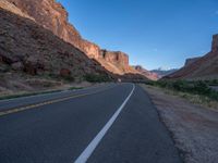 a wide stretch of road between rocky mountains at night time with blue sky and bright light on the side