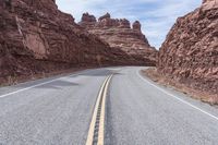 a winding road in the mountains with red rocks behind it and a light brown asphalt