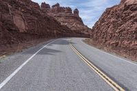 a winding road in the mountains with red rocks behind it and a light brown asphalt