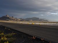 a lone asphalt road in an empty field with mountains in the background and grass on each side