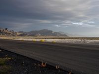 a lone asphalt road in an empty field with mountains in the background and grass on each side