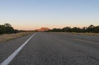 a long empty road with mountains in the distance with a car in the foreground