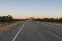 a long empty road with mountains in the distance with a car in the foreground